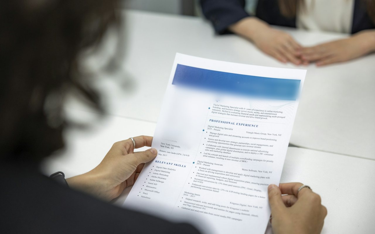 A person reviewing a printed resume across a table (illustrative photo).